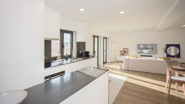 Una cucina moderna con un'isola grande, una zona pranzo con tavolo e sedie in legno e un soggiorno con divano bianco e televisore.
