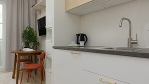 A modern kitchen with white cabinets, a stainless steel sink, and a wooden dining table with two chairs. - Stylish Studio in Wola | Air Conditioning and Balcony (Warszawa)