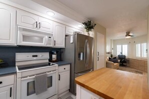 Une cuisine moderne avec des meubles blancs, un réfrigérateur en acier inoxydable, un four à micro-ondes et un plan de travail en bois.