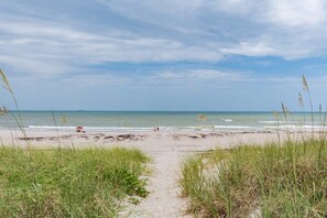 Ein Strandweg, der zum Meer führt, mit grasbewachsenen Dünen an beiden Seiten.