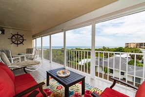 Ein Balkon mit Blick auf den Ozean, weißen Geländern, einem Schiffsschlosselement und einem Tisch mit floralem Teppich.