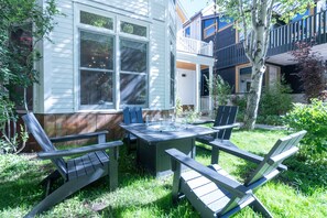 A patio with a table and chairs, a small deck, and a house with a white exterior and a balcony.