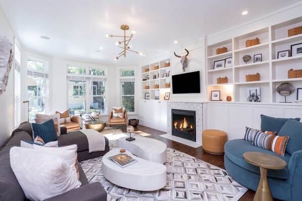 A modern living room with a fireplace, white walls, and a large window.