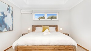 Un dormitorio con cama de madera, ropa de cama blanca, un cojín amarillo y dos lámparas de noche.