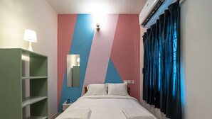 Una cama bien hecha con almohadas, un armario verde, un espejo fijado a la pared y una ventana con cortinas.