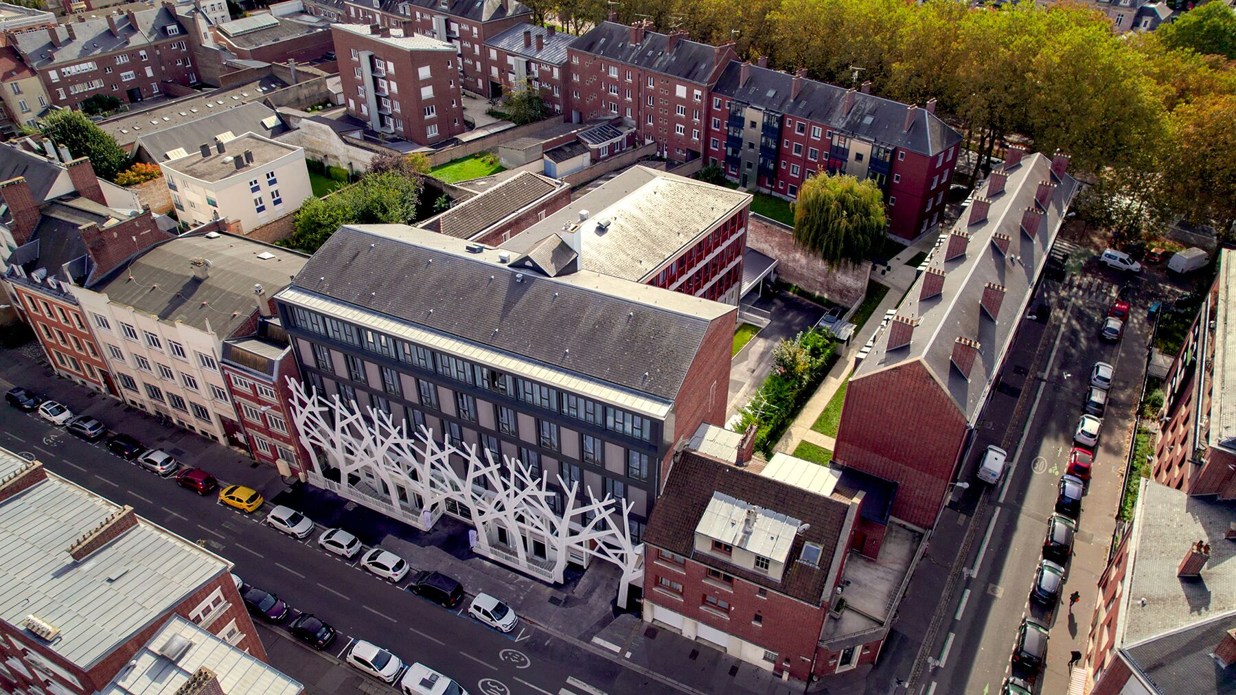 Oversigtsbillede af et bybillede med en markant, moderne bygning med en unik, hvid facade og en traditionel murstensbygning i nærheden.