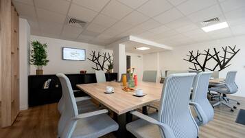 Een vergaderzaal met een houten tafel, grijs gestoffeerde stoelen, een televisiescherm en decoratieve muurkunst.