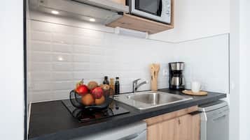 A modern kitchen with a black countertop, stainless steel sink, wooden cabinets, a microwave, a coffee maker, and a fruit basket.