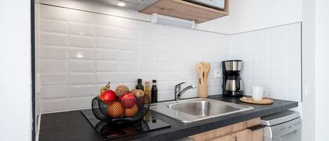 A modern kitchen with a black countertop, stainless steel sink, wooden cabinets, a microwave, a coffee maker, and a fruit basket.
