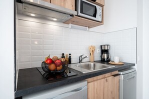 Une cuisine équipée d’un four à micro-ondes, d’une machine à café, d’un évier et d’un panier de fruits.