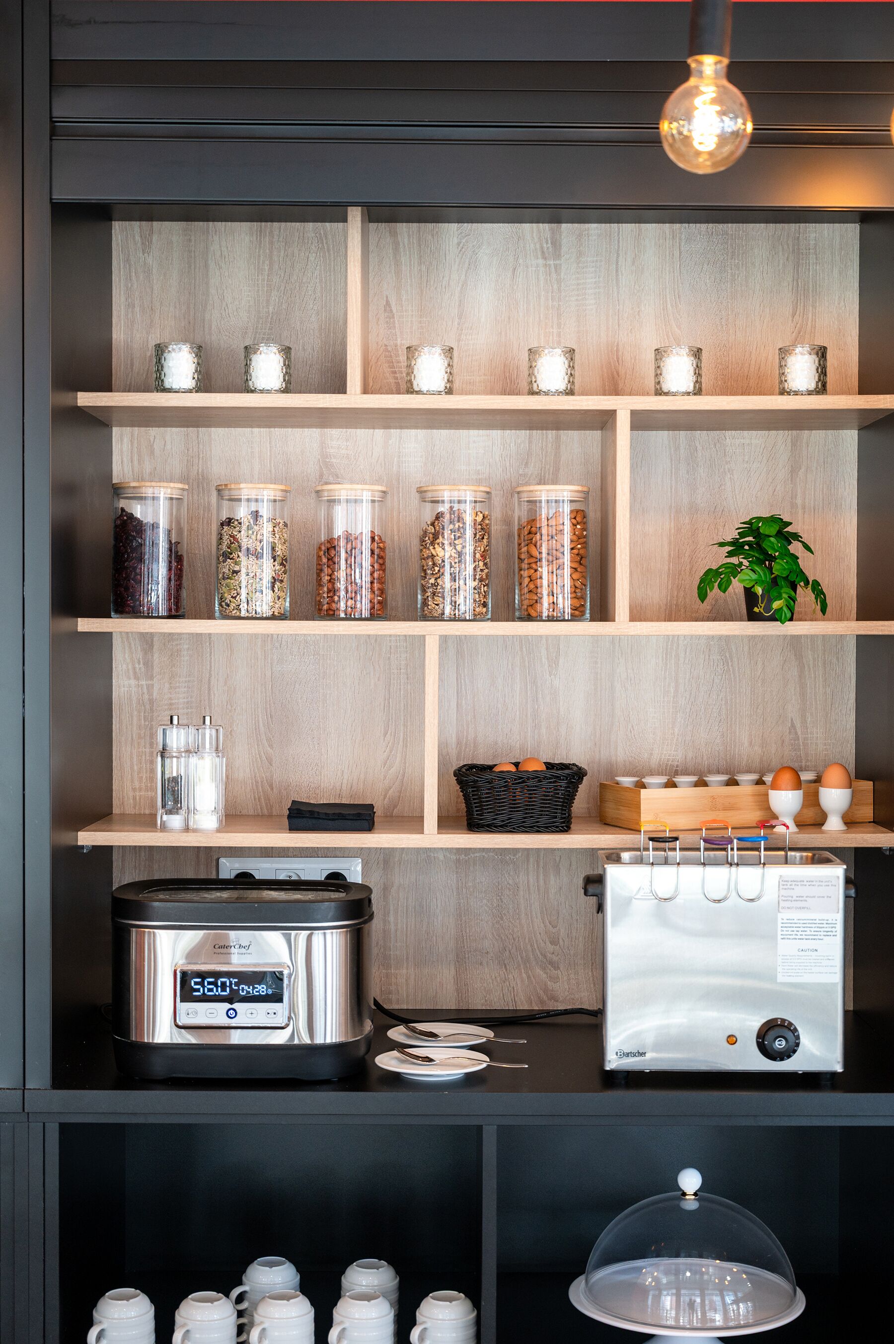 Een keuken met houten planken vol glazen potten met kruiden, een slowcooker en een keukenmachine.