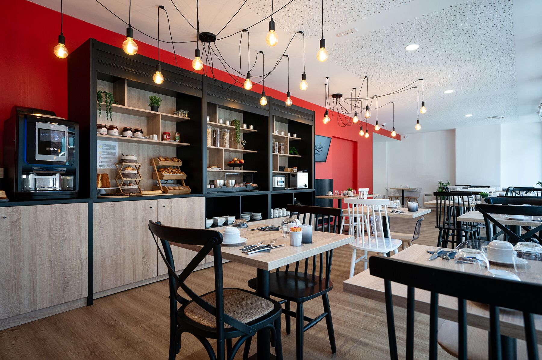 A modern cafe with wooden furniture, a coffee machine, and shelves stocked with pastries and condiments.