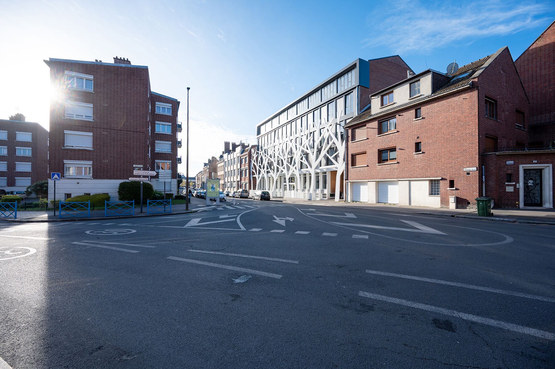 A street with a modern building featuring a unique facade with white structural elements.