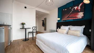 A modern hotel room with a large bed, a desk, and a dining area.