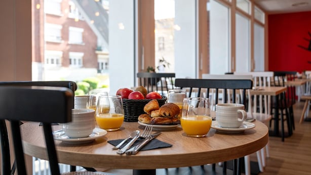 A breakfast table with croissants, apples, and orange juice in a bright room with large windows. - Nemea Appart Hotel Coliseum Amiens Centre (Amiens)