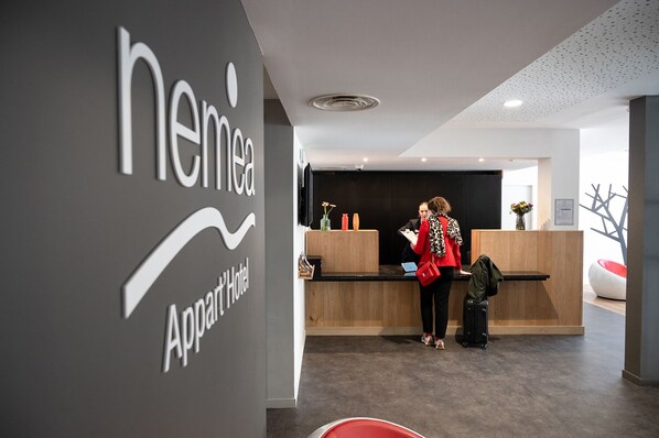 A reception area with a modern design, featuring a reception desk, a wall-mounted sign for 'NEMEA Apartment Hotel', and a clean, contemporary aesthetic. - Nemea Appart Hotel Coliseum Amiens Centre (Amiens)