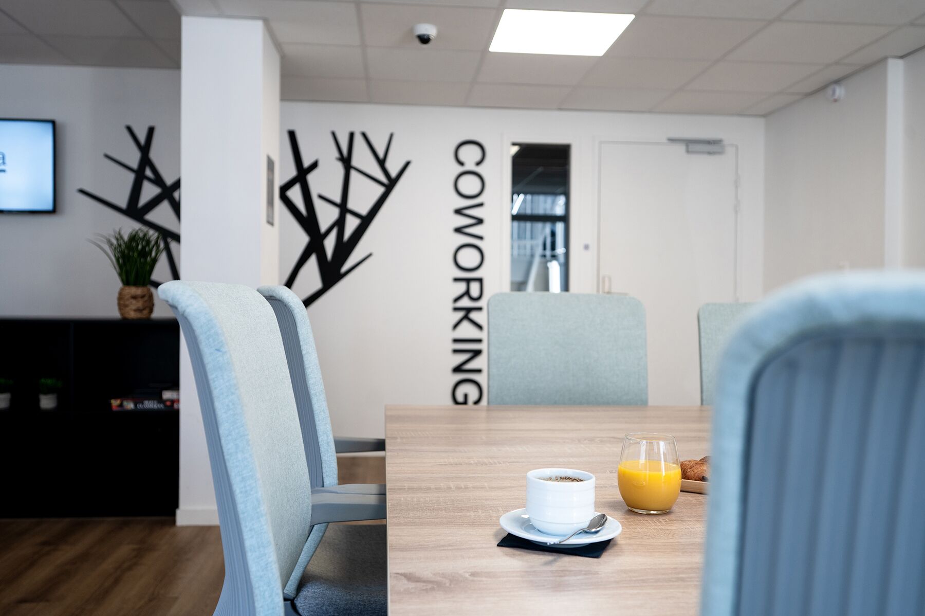 Un espacio de oficina moderno con una mesa de conferencias, sillas, una estación de café y una pared con la palabra 'COWORKING' bien visible.