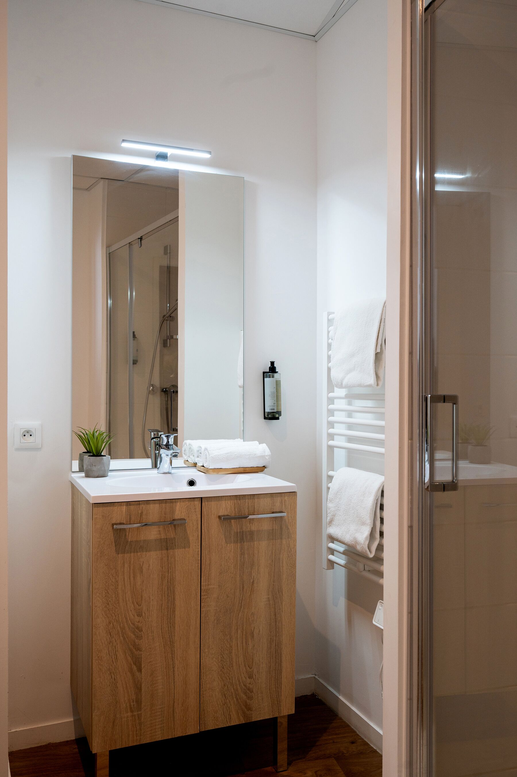 A modern bathroom with a wooden vanity, a large mirror, a shower, and a glass-enclosed shower area.