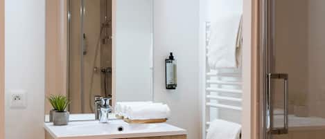 A modern bathroom with a wooden vanity, a large mirror, a shower, and a glass-enclosed shower area.