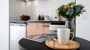 A kitchen with white cabinets, a black countertop, and a vase with flowers on a wooden coaster. - Nemea Appart Hotel Coliseum Amiens Centre (Amiens)