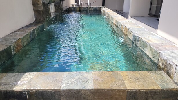 A rectangular swimming pool with clear water, surrounded by stone tiles and a stone wall. - Brand new Private self catering Apartment situated in Flic en Flac (Flic en Flac)