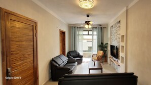 A modern living room with a sofa, chairs, a TV, and a ceiling fan. - Brand new Private self catering Apartment situated in Flic en Flac (Flic en Flac)