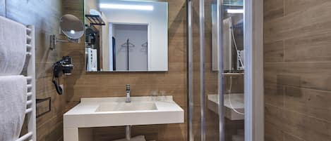 A modern bathroom with a white sink, mirror, and glass shower enclosure.