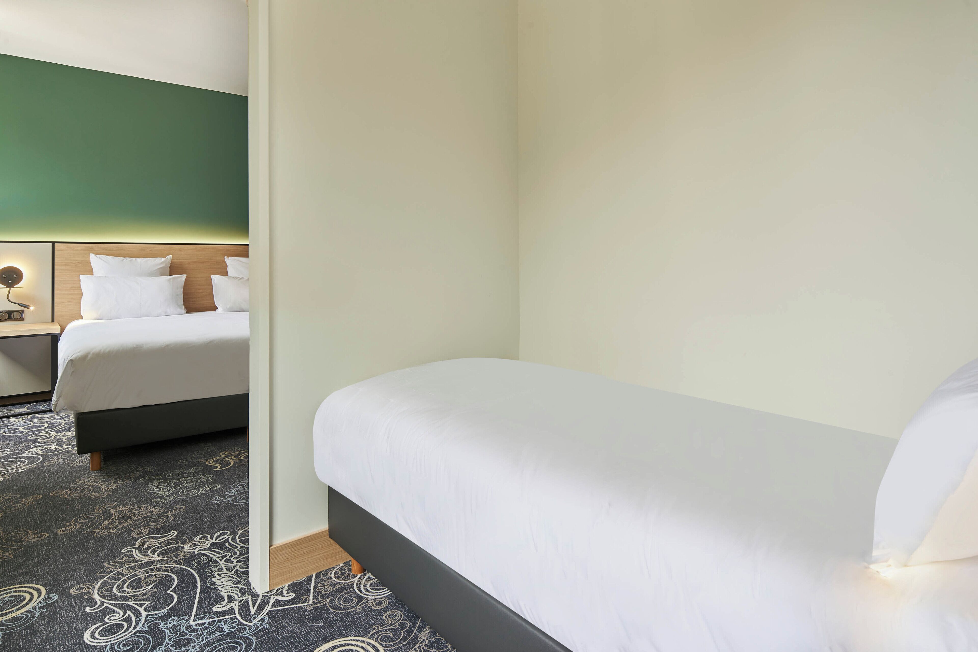 Una habitación de hotel con una cama, una mesita de noche y una lámpara de pared.