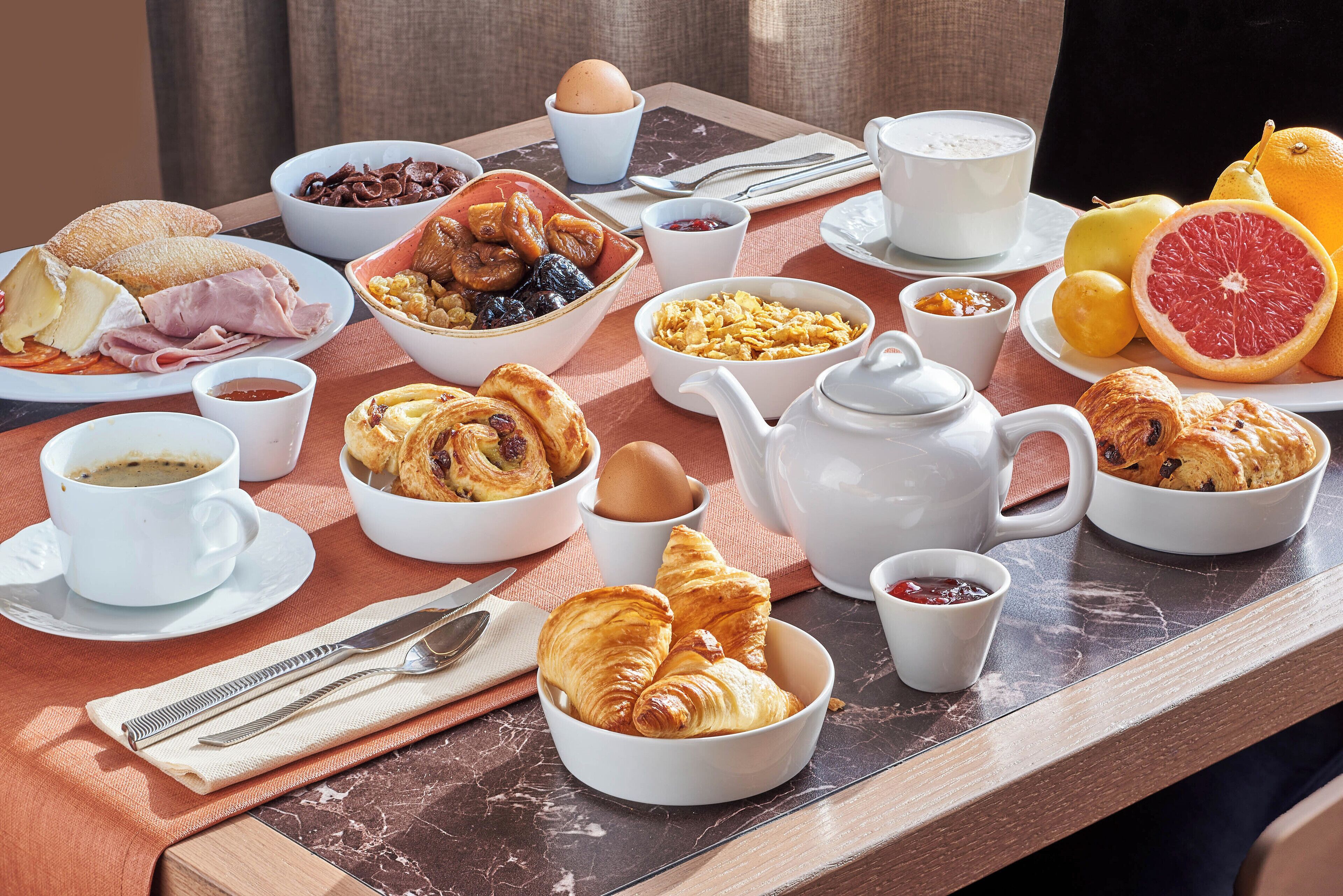 A breakfast table with various food items, including pastries, fruits, and beverages.
