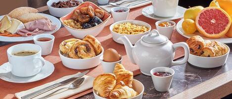 A breakfast table with various food items, including pastries, fruits, and beverages.