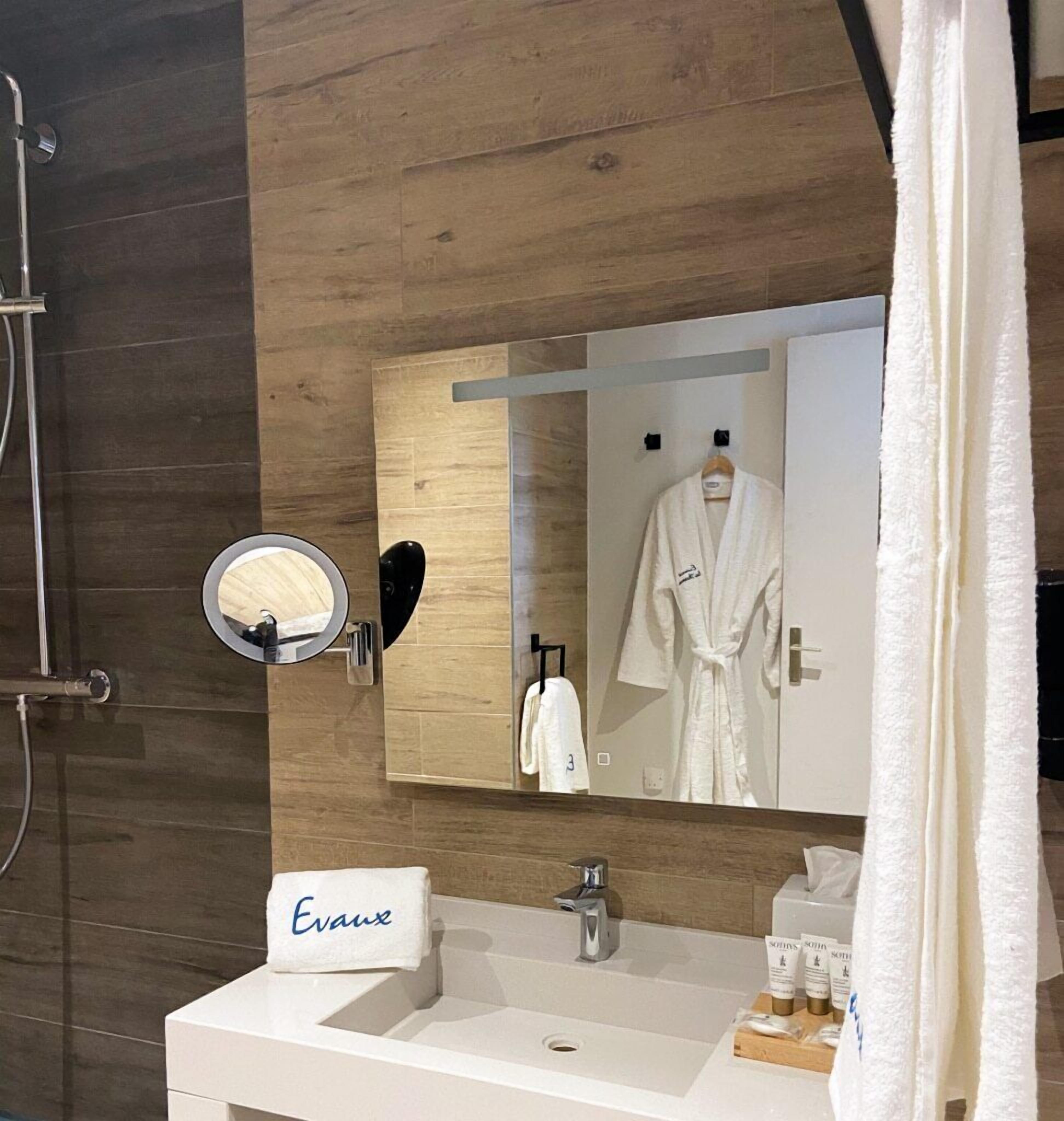 A modern bathroom with a wooden wall, a white sink, a mirror, and a robe hanging on a rack.