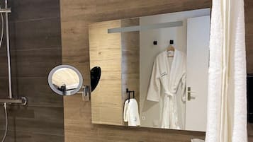 A modern bathroom with a wooden wall, a white sink, a mirror, and a robe hanging on a rack.