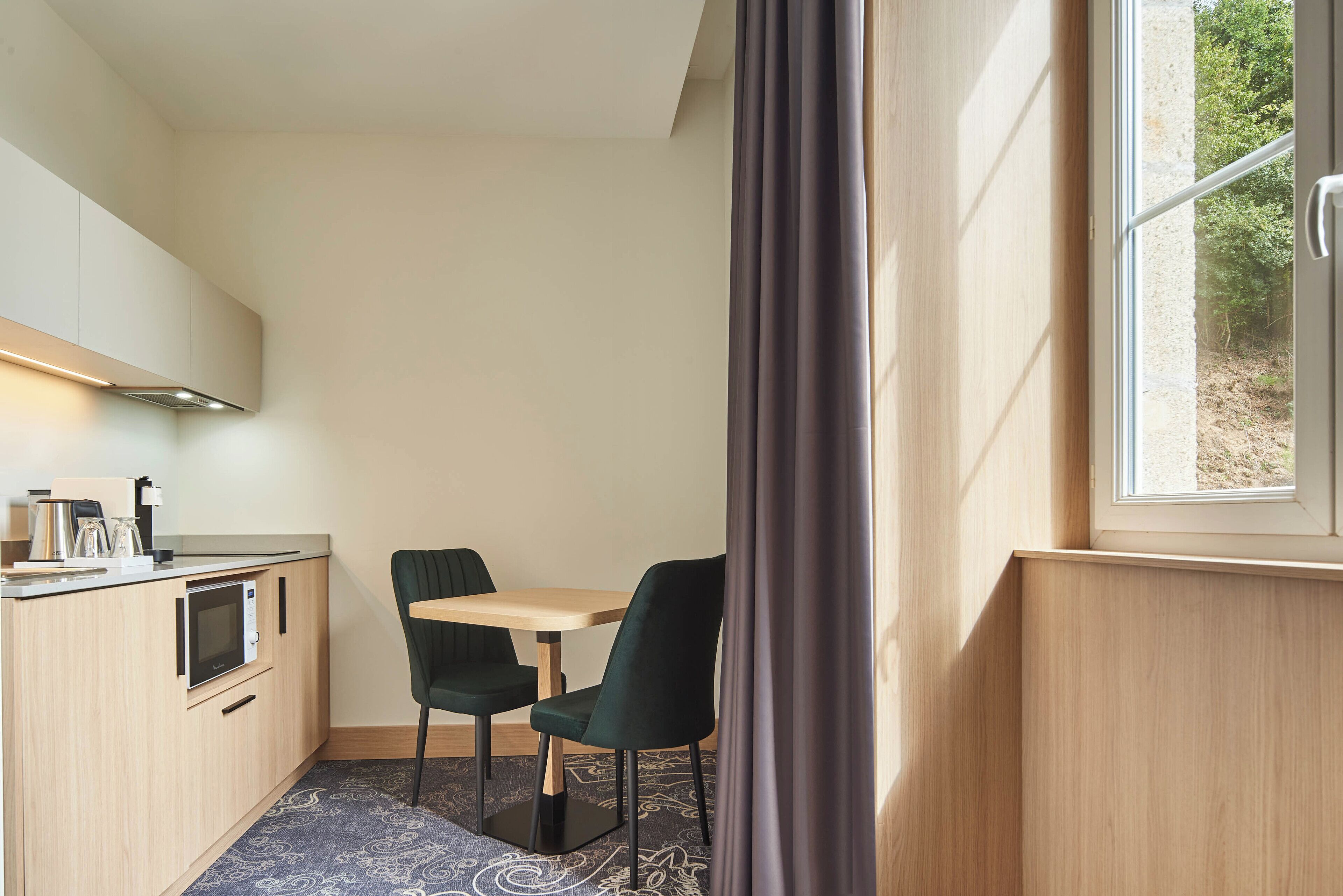 A compact kitchen with a microwave, a small sink, and a window with curtains.