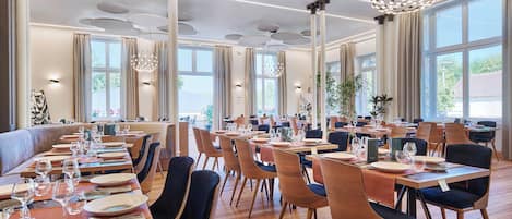 Un comedor amplio con varias mesas y sillas, ventanas grandes y luminarias modernas.