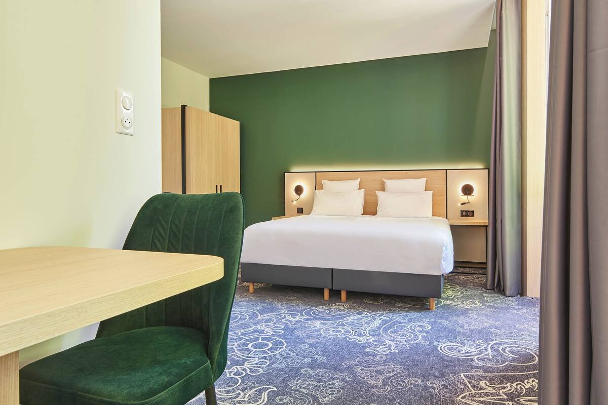 Habitación de hotel con cama, escritorio, silla, armario y alfombra estampada.