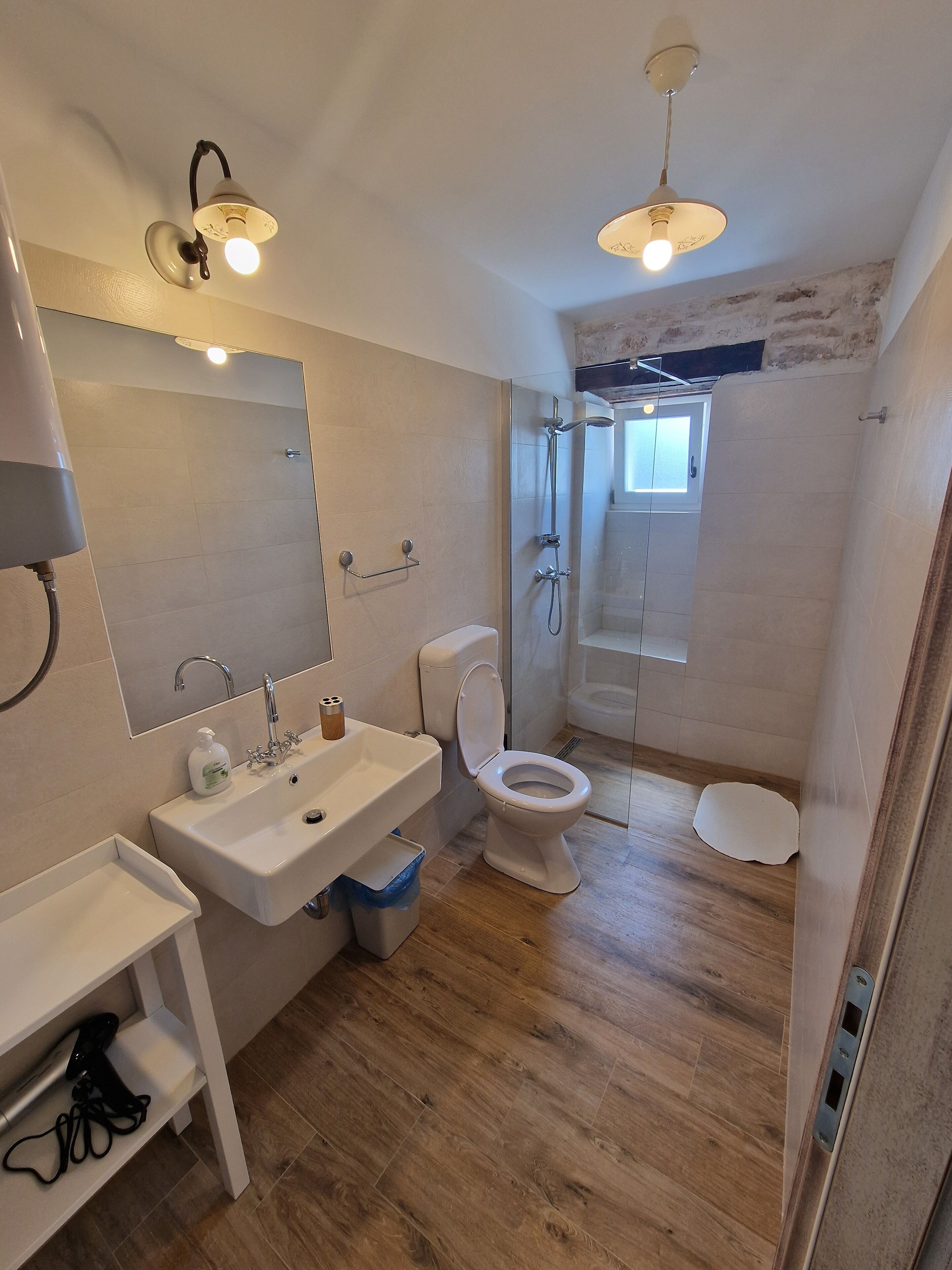 A modern bathroom with a wooden floor, a white sink, a toilet, and a shower area.