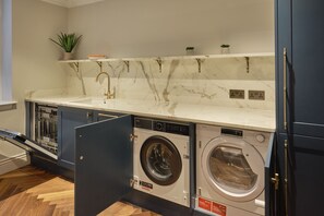 A modern kitchen with marble countertops, built-in dishwasher, and a double washing machine. - Mayfair Darley House by Viridian Apartments (London)