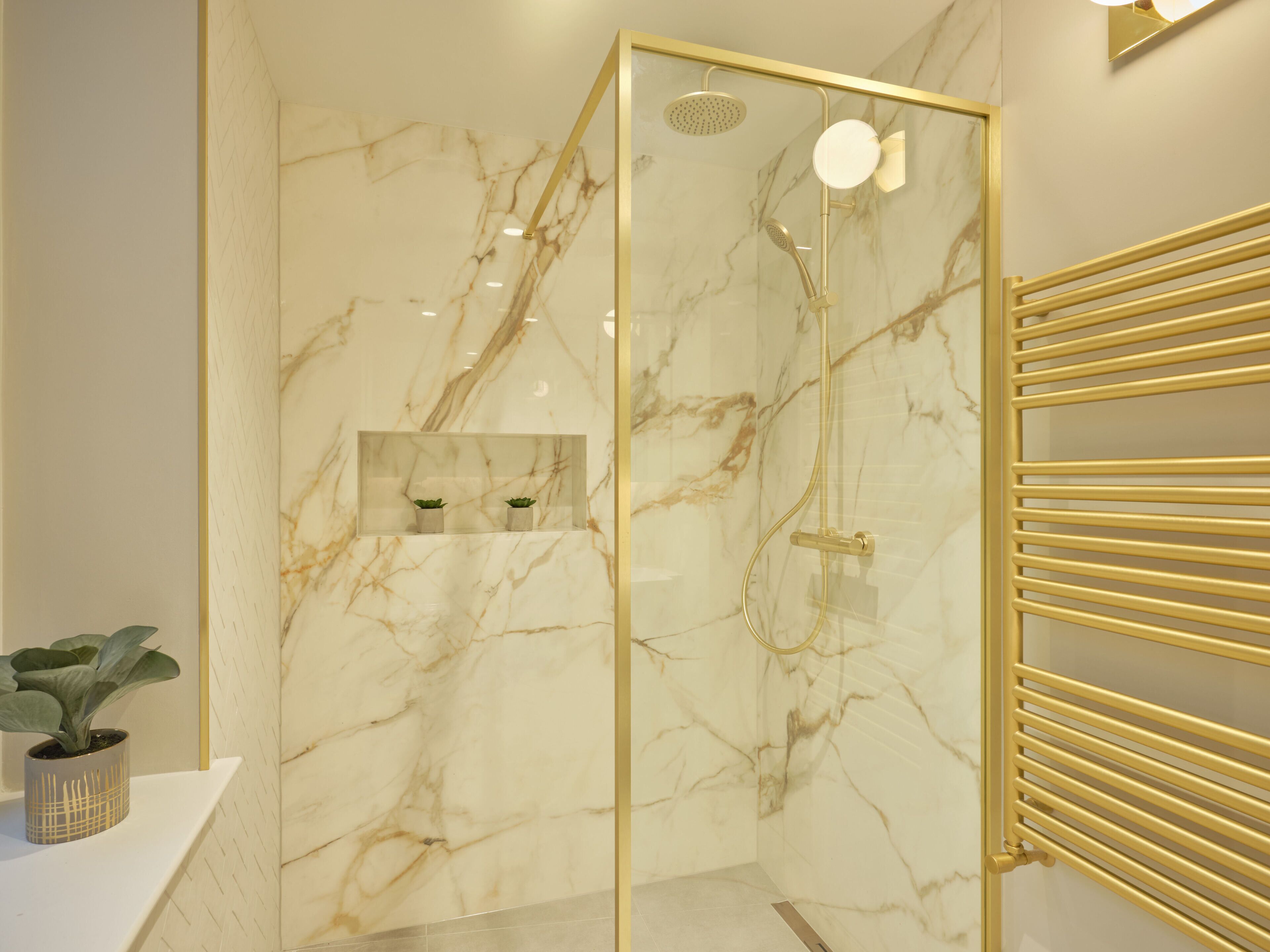 A modern bathroom with a glass-enclosed shower, marble walls, and a gold-framed mirror.