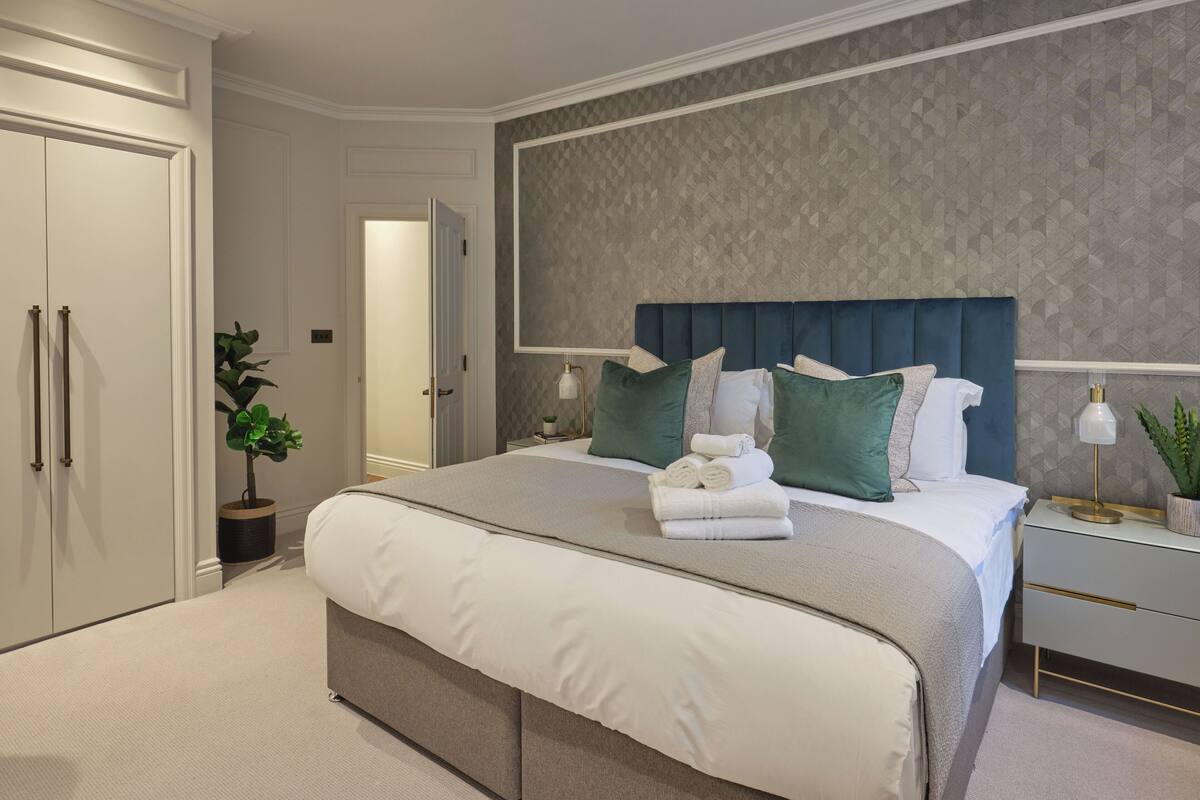 A modern bedroom with a large bed, a nightstand, a dresser, and a potted plant.