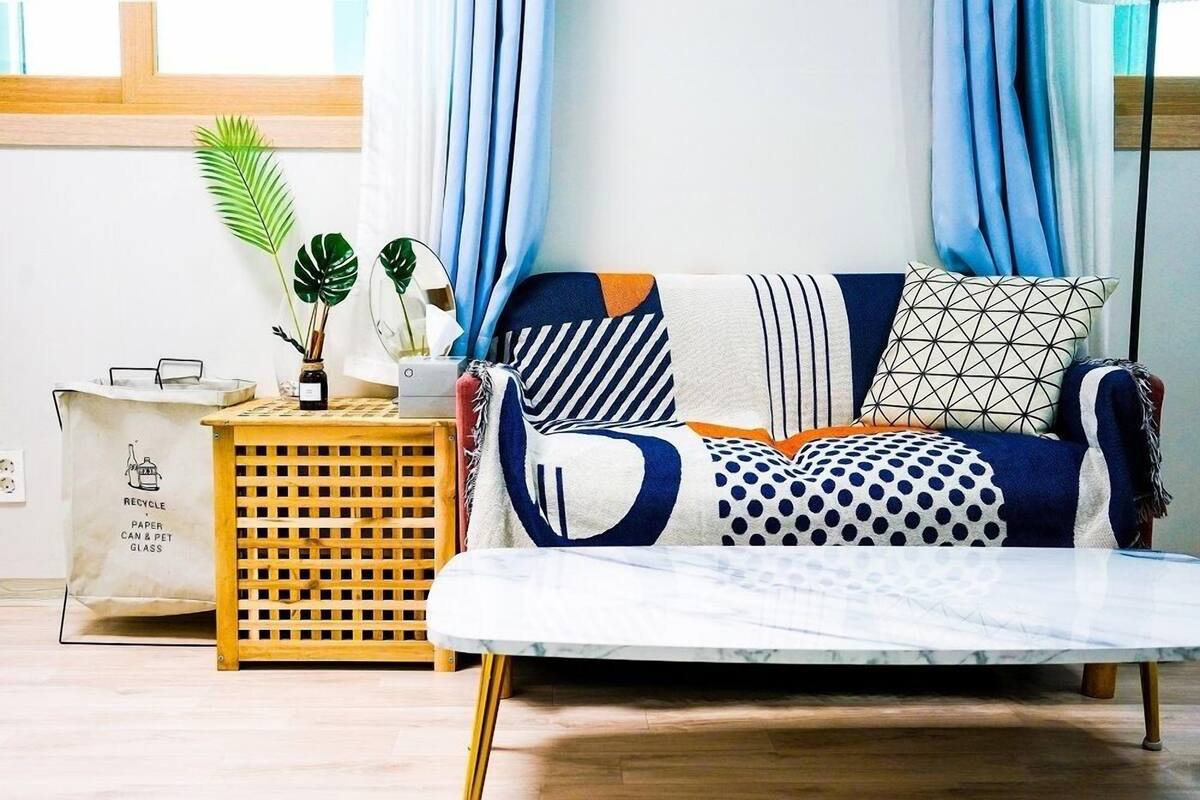 A living room with a sofa, a coffee table, a side table with a plant, and a recycling bag.