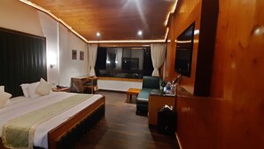 A hotel room with a large bed, a desk with a chair, a TV, and a window with curtains. - THE NORTH STAR HOTEL (Gangtok)