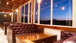 A row of leather sofas and glass-top tables in a room with large windows and wooden ceiling. - THE NORTH STAR HOTEL (Gangtok)