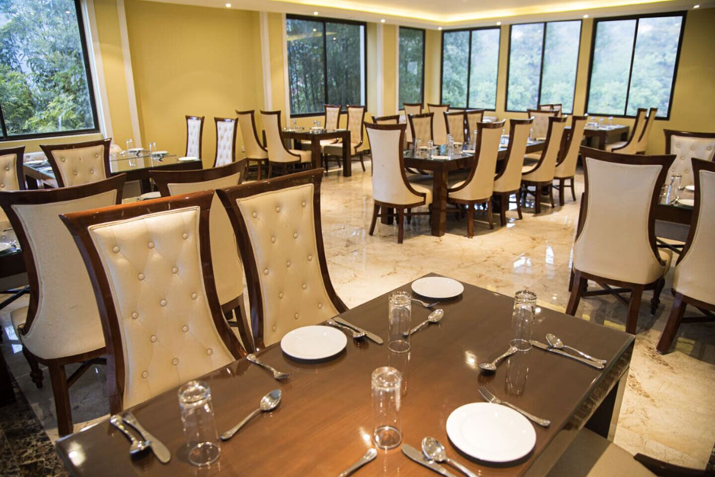 A dining area with multiple tables and chairs, arranged in a spacious layout with large windows providing natural light.
