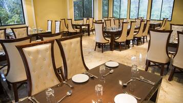 A dining area with multiple tables and chairs, arranged in a spacious layout with large windows providing natural light.