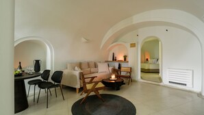 Un salon moderne avec un canapé, des fauteuils, une table basse et un téléviseur. Des arches servent de passages vers les autres pièces.