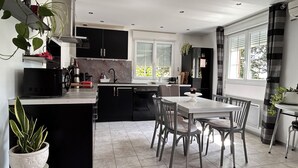 Uma cozinha moderna com armários pretos, uma área de jantar com mesa e cadeiras brancas, e uma janela grande que oferece iluminação natural.