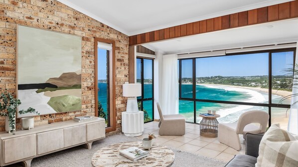 A spacious living room with a large painting, a wooden cabinet, and a view of the ocean.