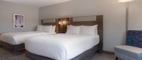 A hotel room with two beds, a seating area, and a wall-mounted light fixture.