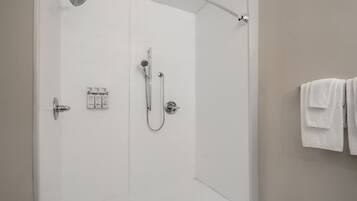 Een moderne badkamer met een glazen douchedeur, een handdouche, een wandmengkraan en een handdoekrek met handdoeken.