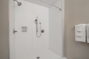 A modern shower room with a glass door, a handheld showerhead, a wall-mounted faucet, and a towel rack with towels. - Holiday Inn Express and Suites Oscoda by IHG (Oscoda)
